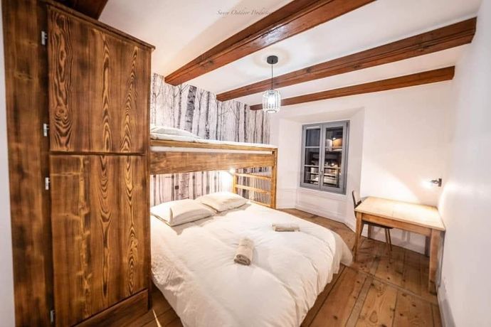 Chambre cosy avec mobilier en bois : lit superposé, armoire, bureau, fenêtre et poutres apparentes.