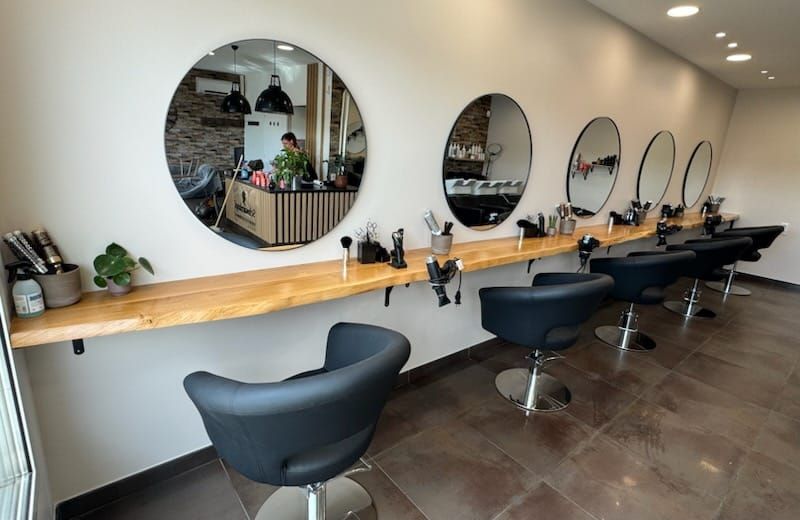 Intérieur de salon de coiffure avec miroirs circulaires, chaises noires, étagère en bois et outils.