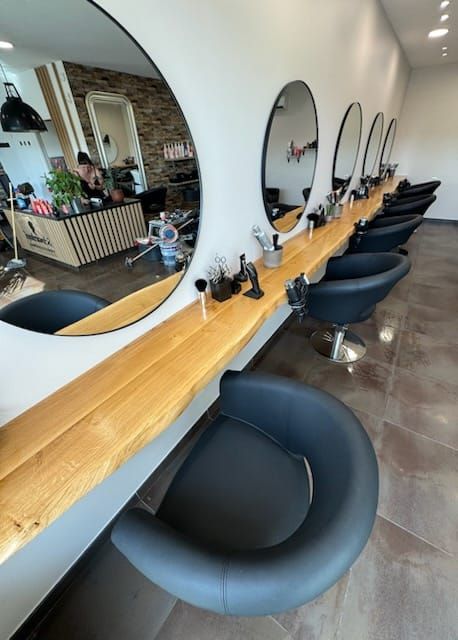 Intérieur de salon de coiffure avec miroirs, postes de travail et chaises noires. Comptoir et parquet en bois.
