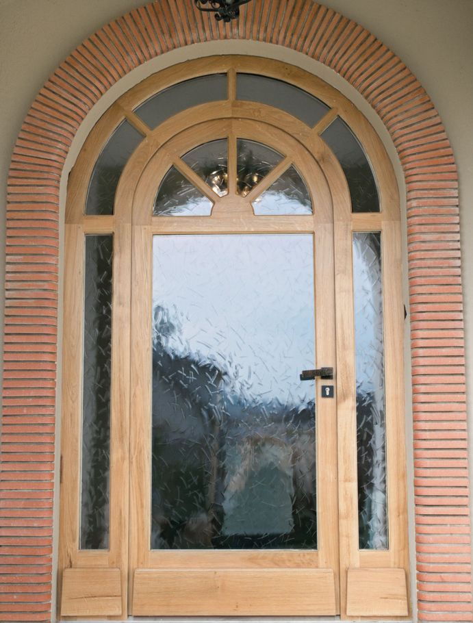 Porte d'entrée en bois cintrée avec encadrement en brique et verre texturé.