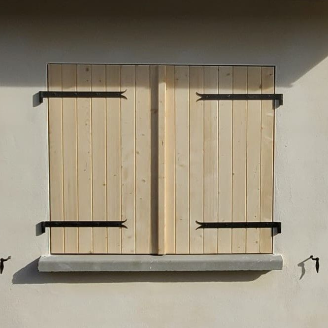 Volets en bois fermés sur un bâtiment de couleur claire, maintenus par une quincaillerie en métal noir.