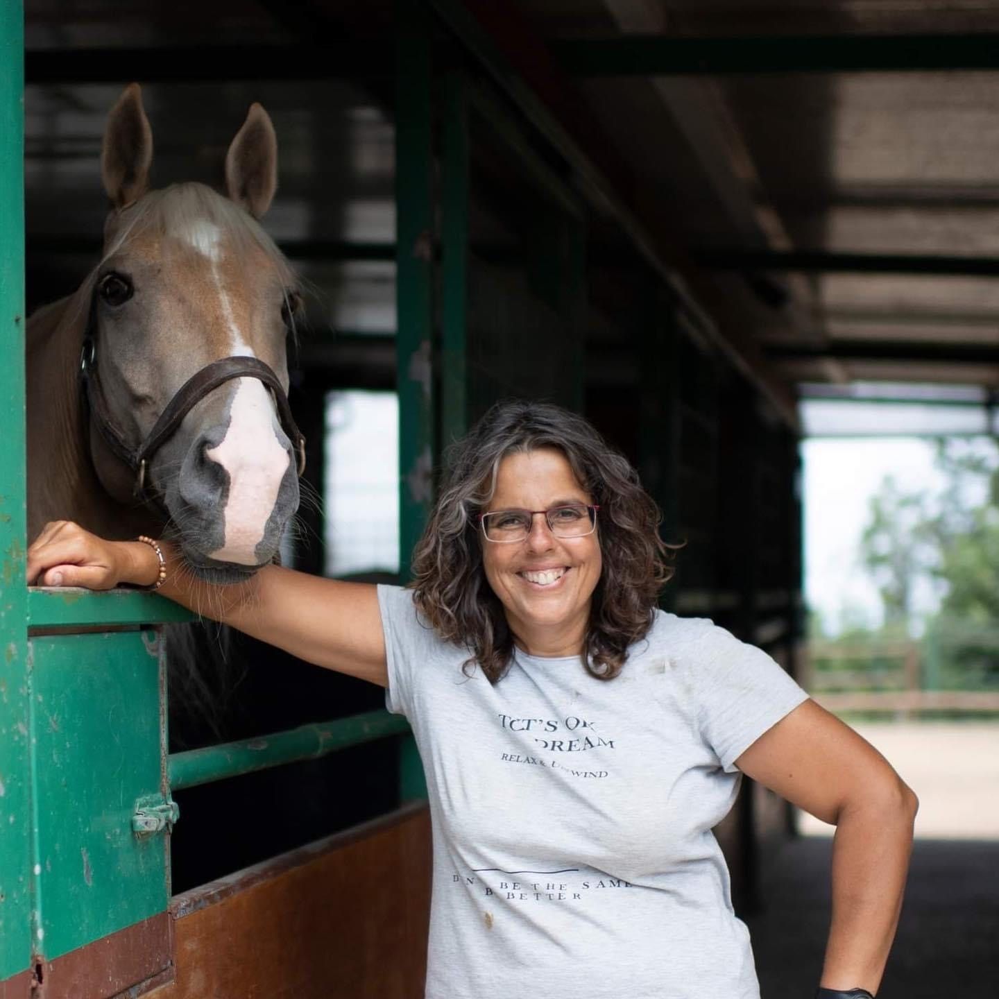 Una mujer parada junto a un caballo en un establo con una camiseta que dice 