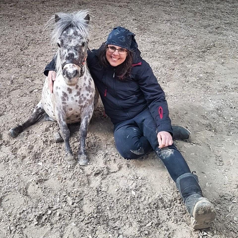 Una mujer está sentada en el suelo junto a un pequeño pony.