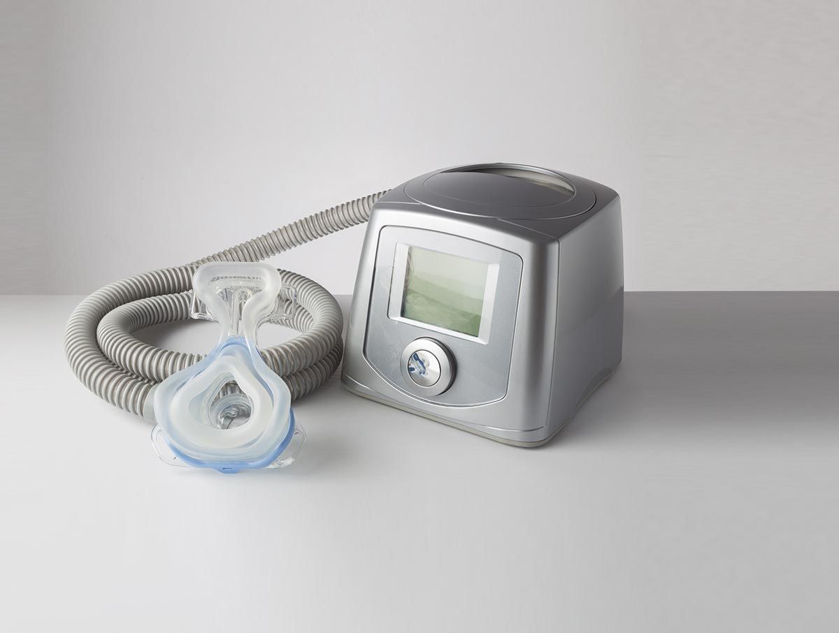 Una máquina CPAP con una máscara adjunta está sobre una mesa.