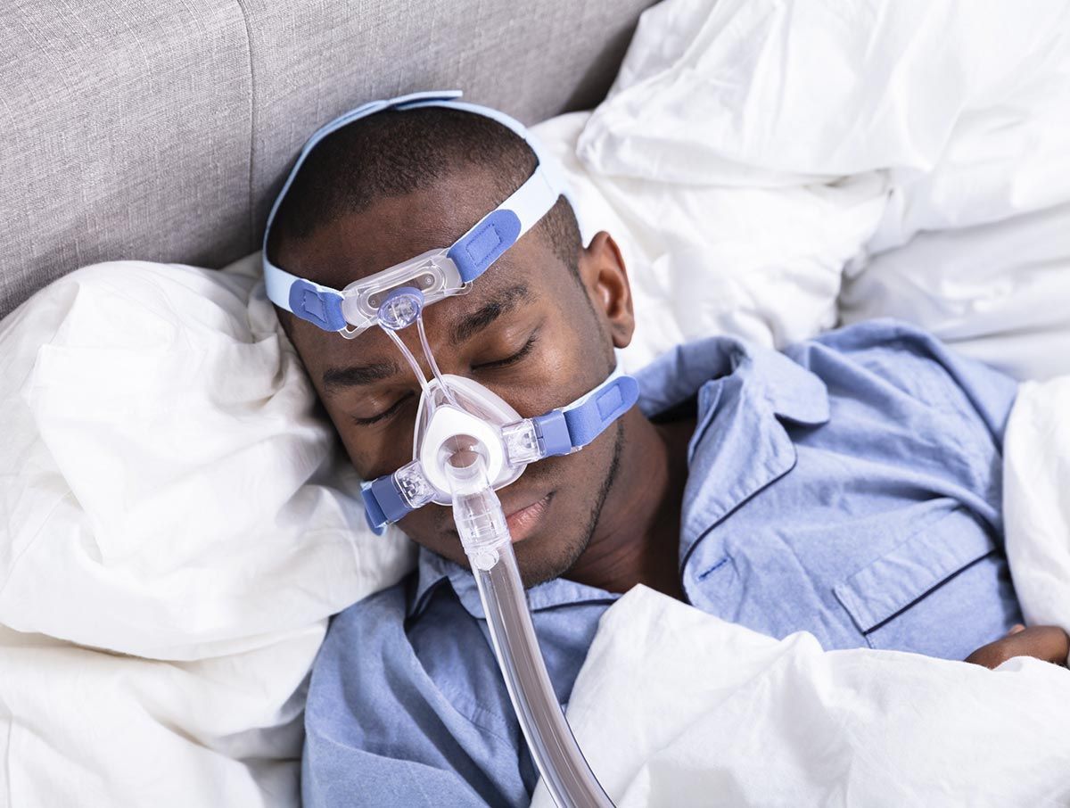 Un hombre está durmiendo en la cama con una máscara CPAP en la cara.
