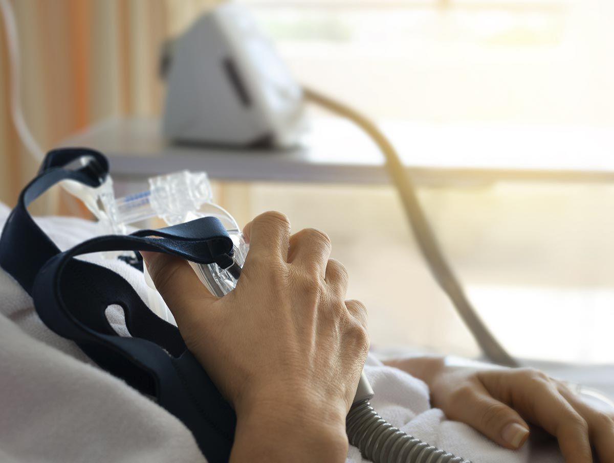 Una persona está acostada en una cama de hospital con una máscara de oxígeno en la cara.