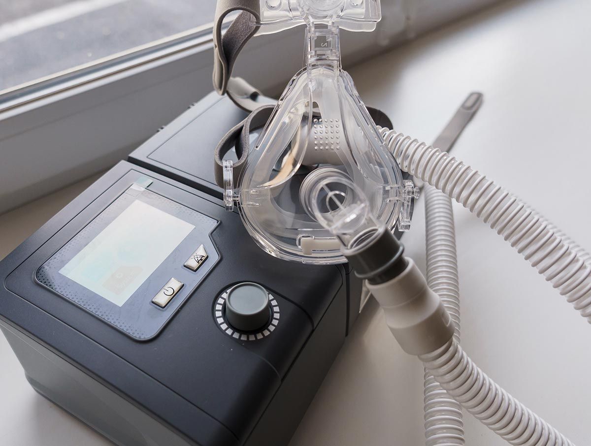 Una máquina CPAP está sobre una mesa al lado de una ventana.
