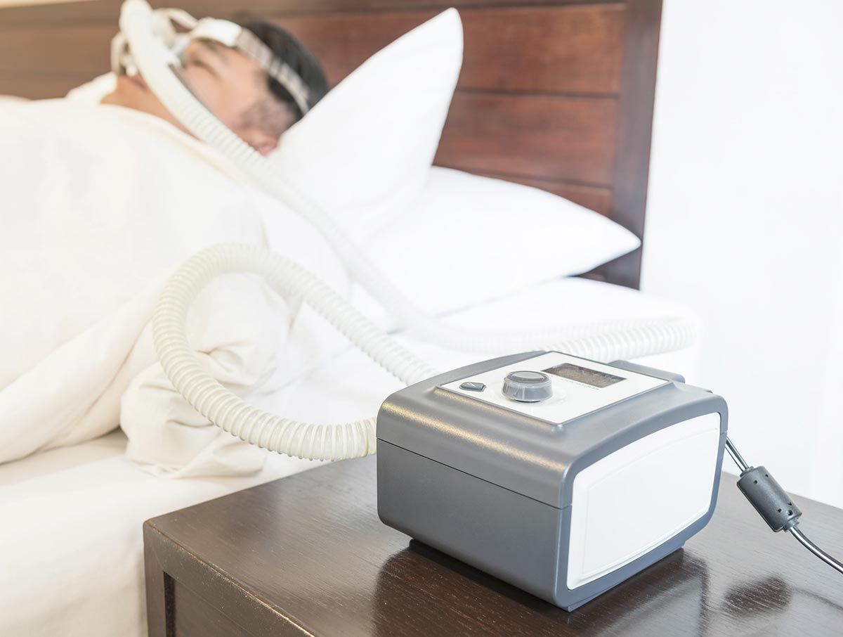 Un hombre está durmiendo en una cama con una máquina CPAP en una mesita de noche.