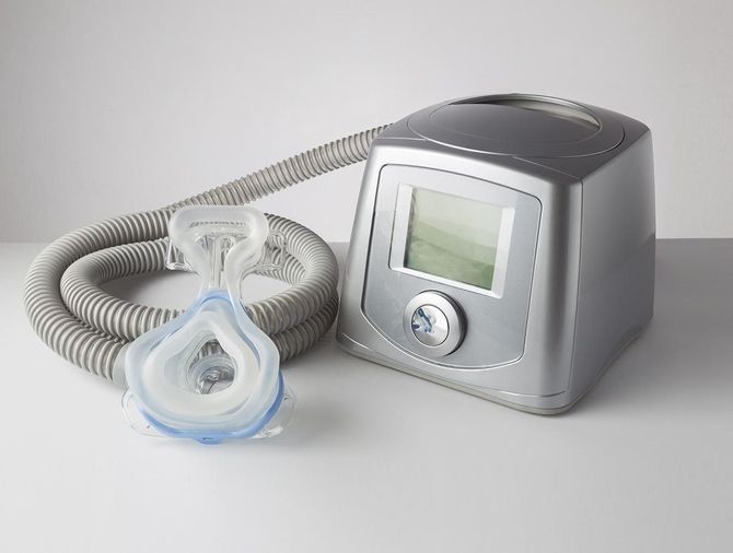 Una máquina CPAP con una máscara adjunta está sobre una mesa.