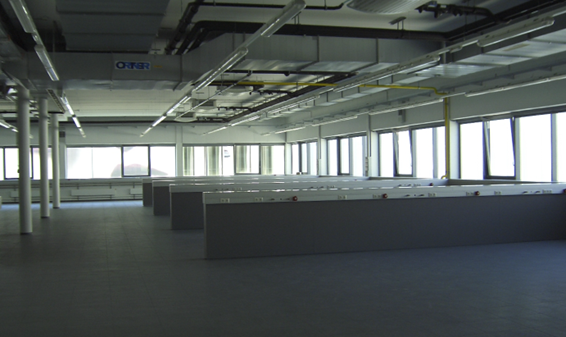 Blick in ein leeres, modernes Großraumbüro mit sichtbaren Lüftungskanälen an der Decke.