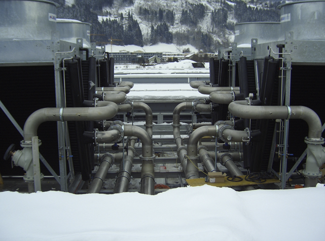 Eine Nahaufnahme von zwei industriellen Kühltürmen mit komplexen Rohrverbindungen in einer winterlichen Umgebung.