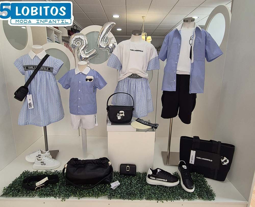 Un escaparate que presenta ropa infantil en azul y blanco, incluidas camisas, vestidos y accesorios como zapatos y bolsos.