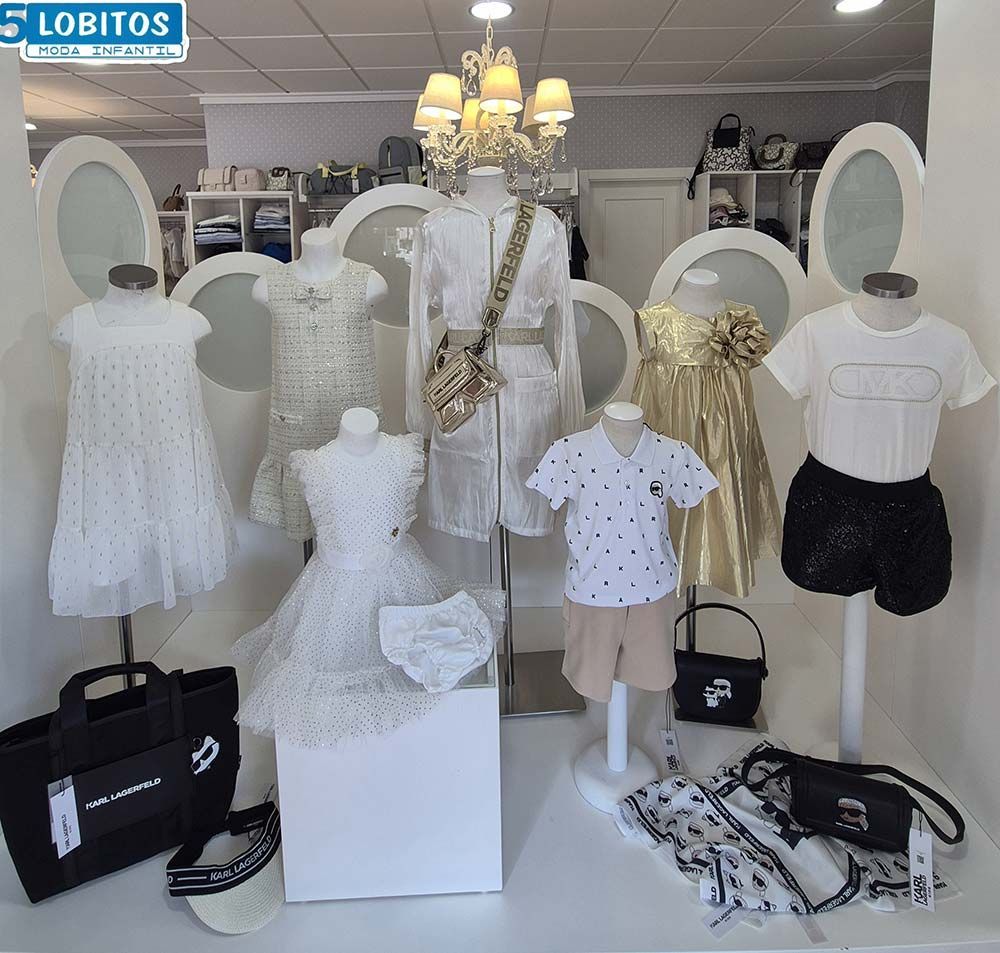 Exhibición de ropa infantil: vestidos, shorts y camisetas en blanco, dorado y lunares. Accesorios: bolsos y sombreros.