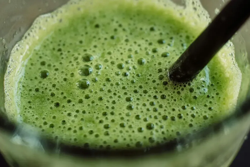 Primer plano de un batido verde espumoso en un vaso con una pajita negra.