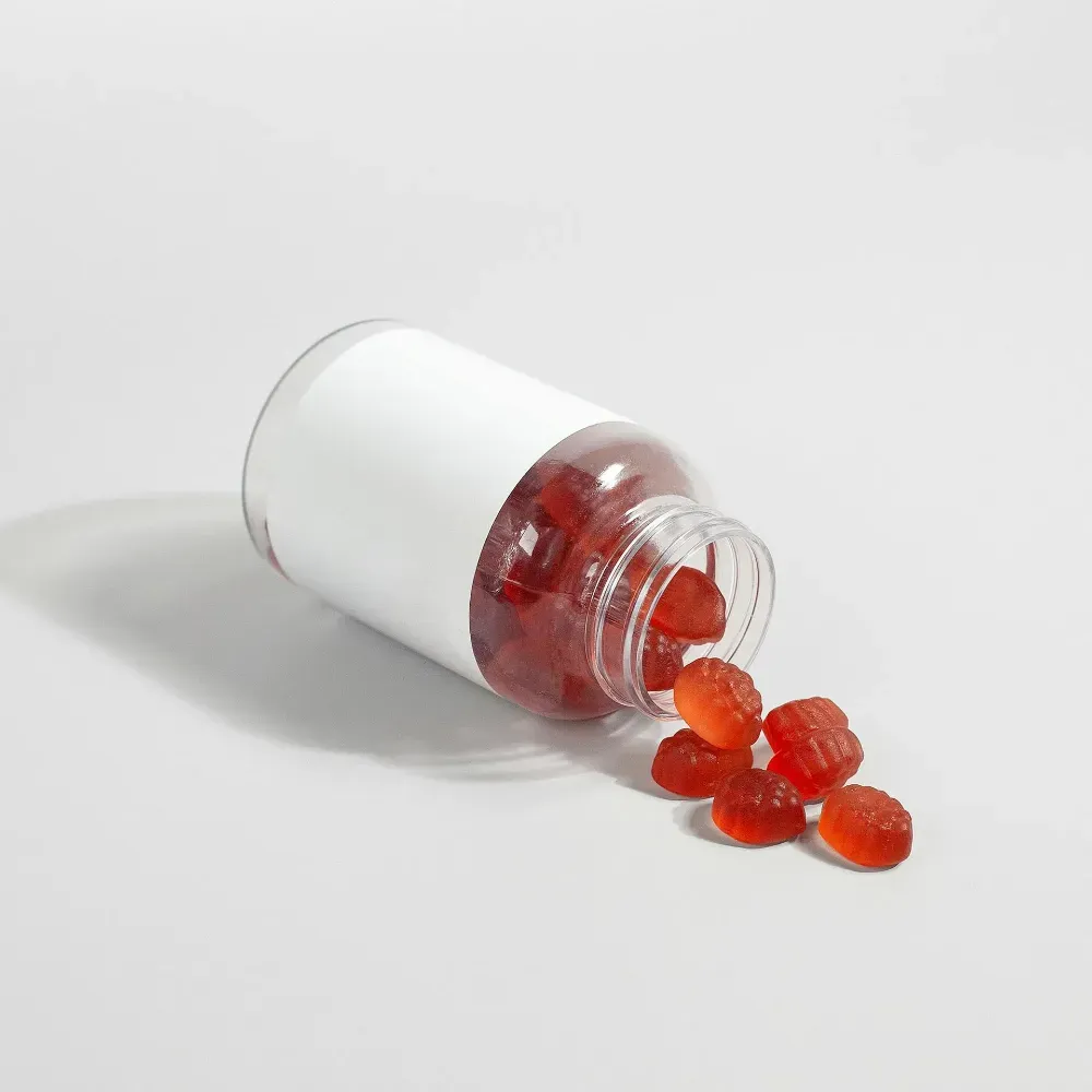 Frasco de pastillas blanco derramado con cápsulas rojas sobre una superficie blanca.