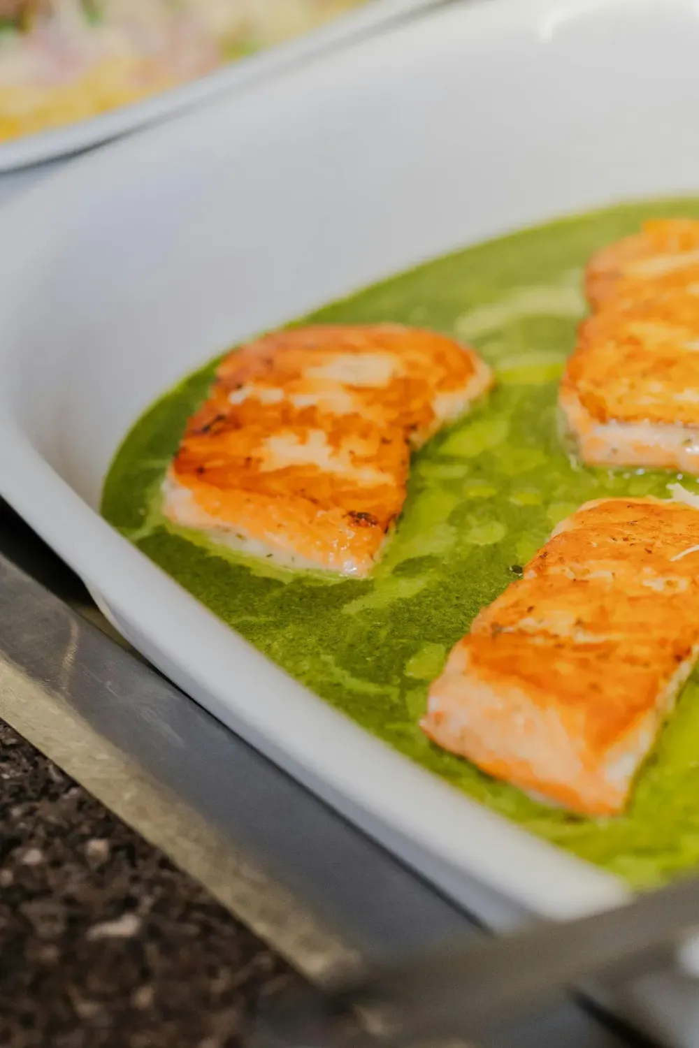 Filetes de salmón a la parrilla con salsa verde en una fuente blanca.