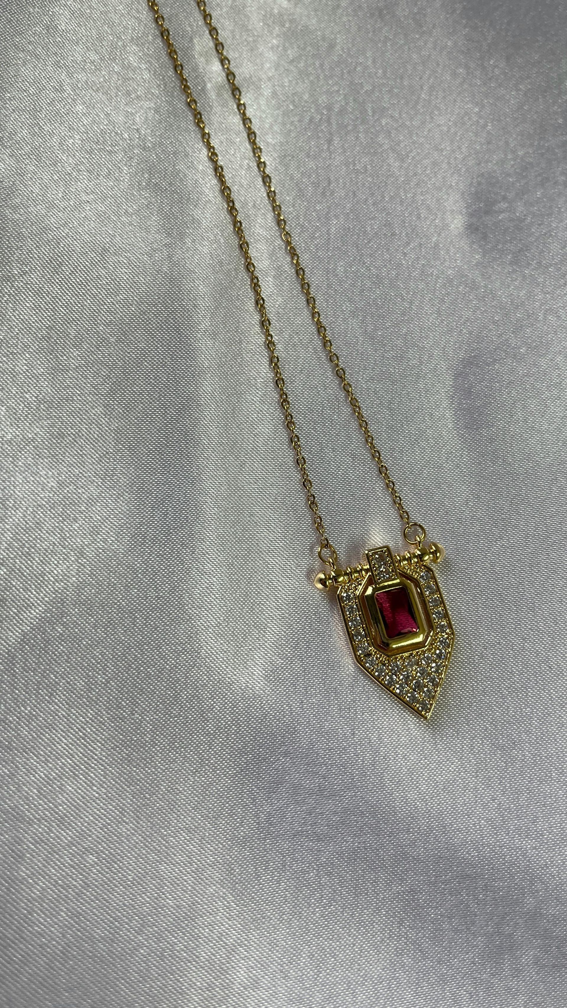 Collar de oro con un colgante rojo en forma de corazón sobre un fondo de tela blanca texturizada.