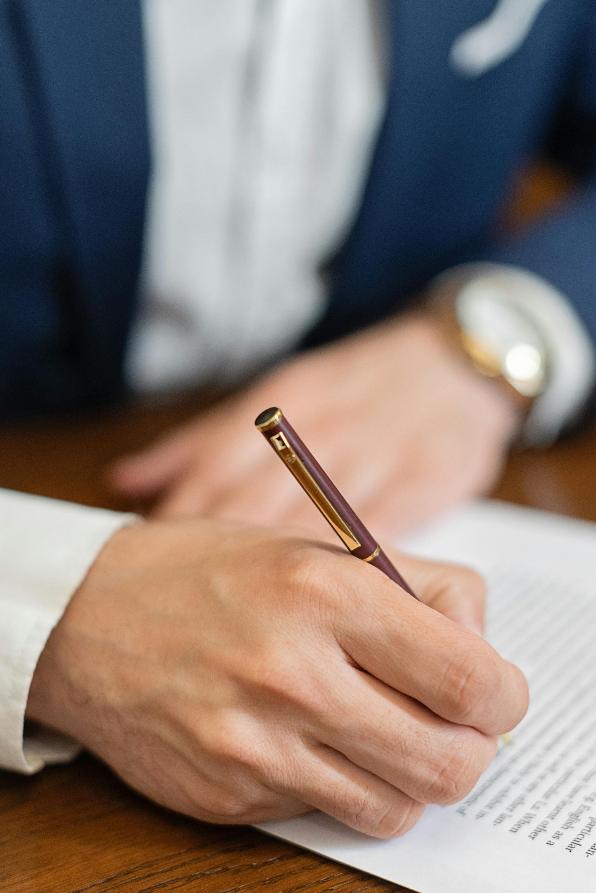 Escritura a mano en un documento en un escritorio, con la manga de un traje azul visible.
