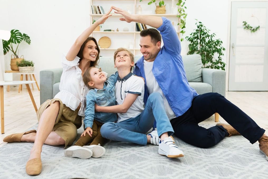 Une famille se tient la main, formant un toit symbolique, assise à même le sol à l'intérieur.