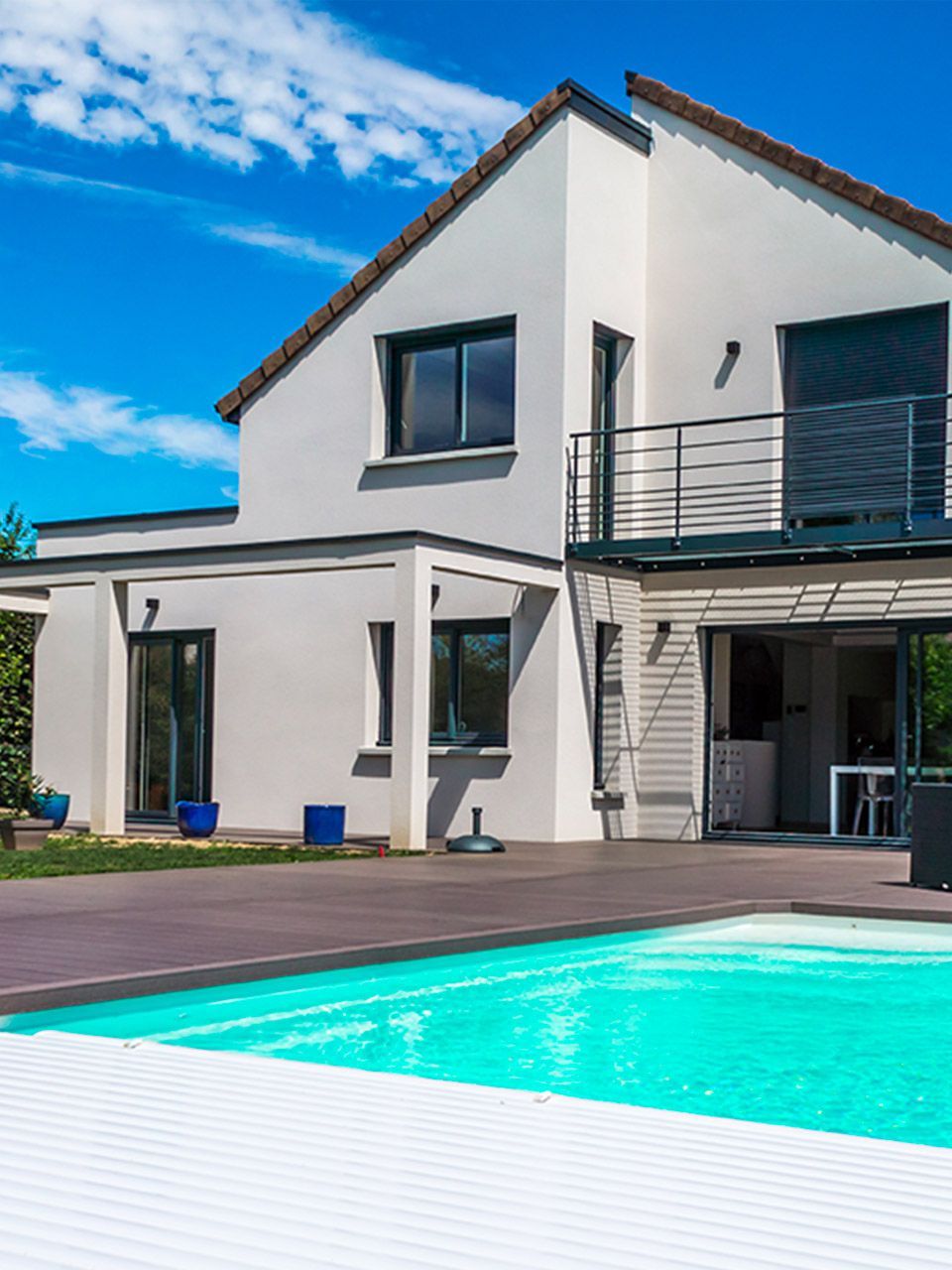 Maison moderne à étage avec toit classique et toit plat et une grande terrasse en bois autour d'une piscine.