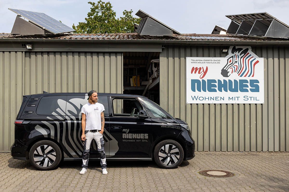 Mann steht neben schwarzem Lieferwagen mit Zebrastreifen vor einem Gebäude mit dem Logo „my NIEHUES“.