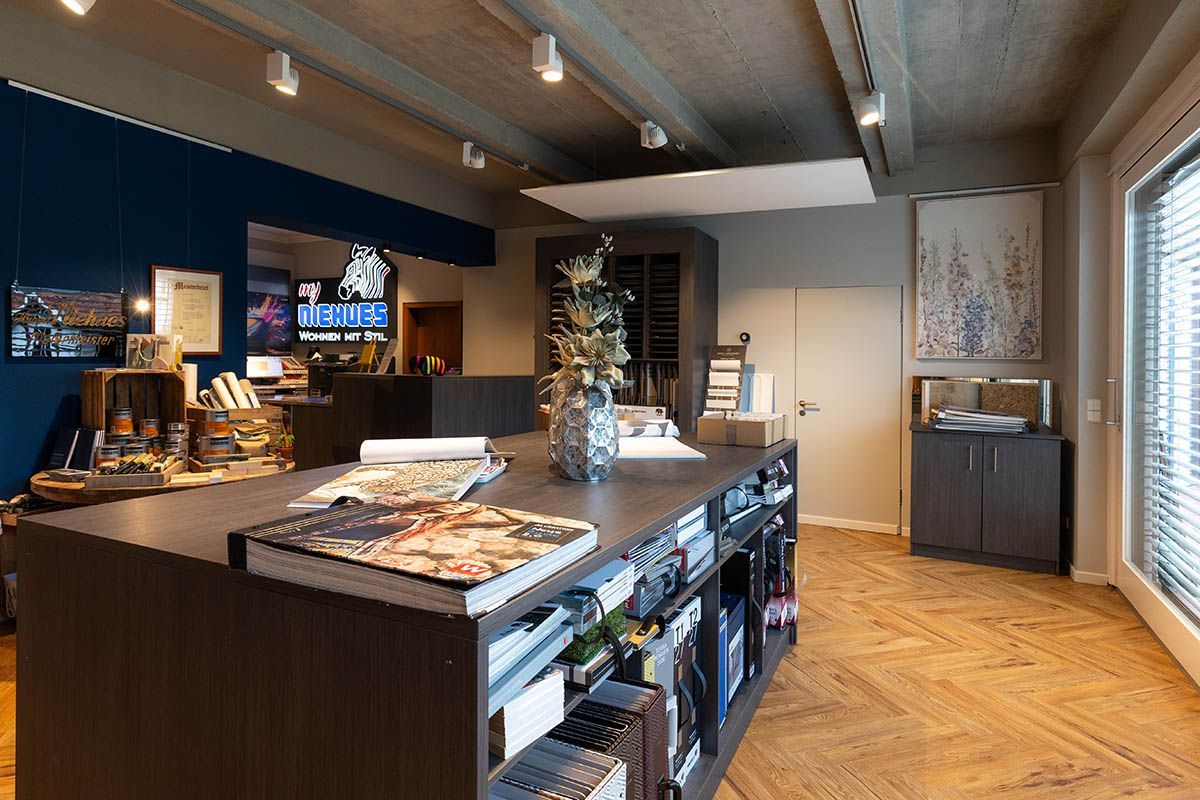 Ein Verkaufsraum mit einer großen dunkelbraunen Ausstellungsinsel. Blaue Wand, weiße Kunst und Holzdecke.