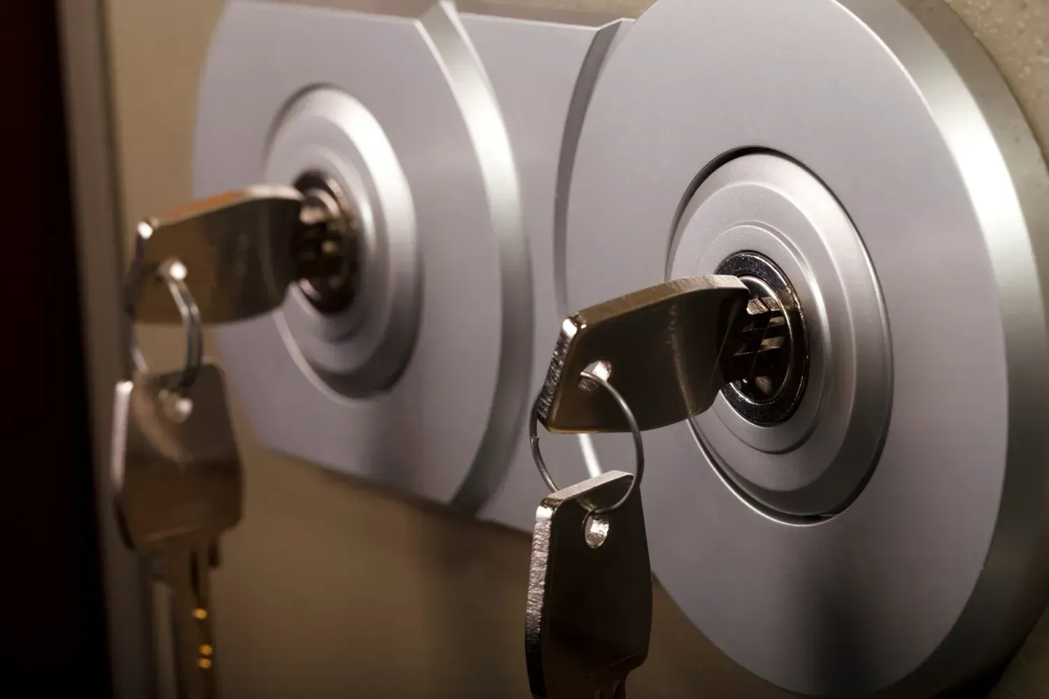 Dos cilindros de cerradura circulares de plata, uno al lado del otro en una pared, cada uno con una llave de metal