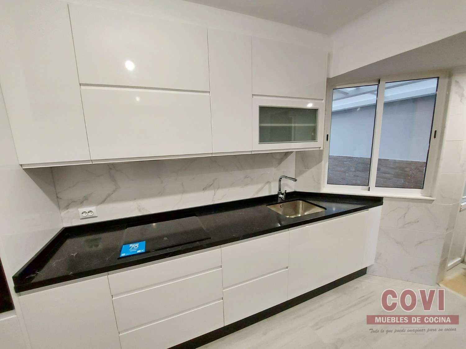 Cocina moderna blanca con encimera negra y ventana.