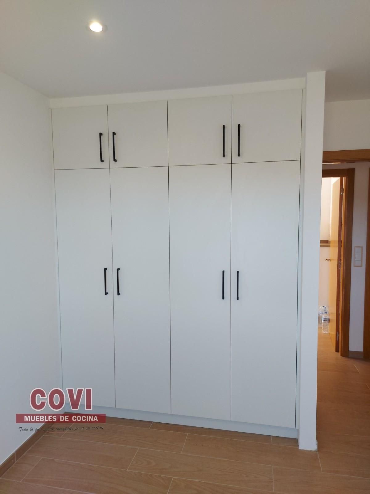 Armario empotrado de color blanco con tiradores de color negro en una habitación con puerta de entrada.