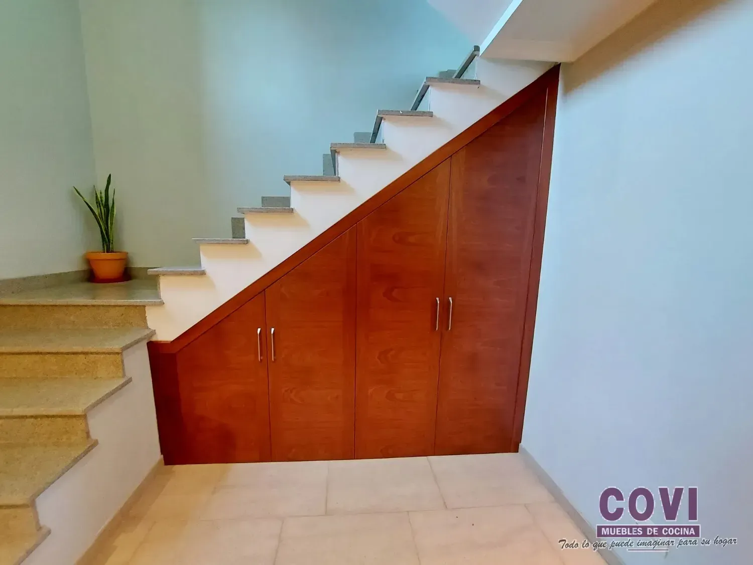 Armarios de madera empotrados bajo la escalera. Escalones y paredes de piedra clara.