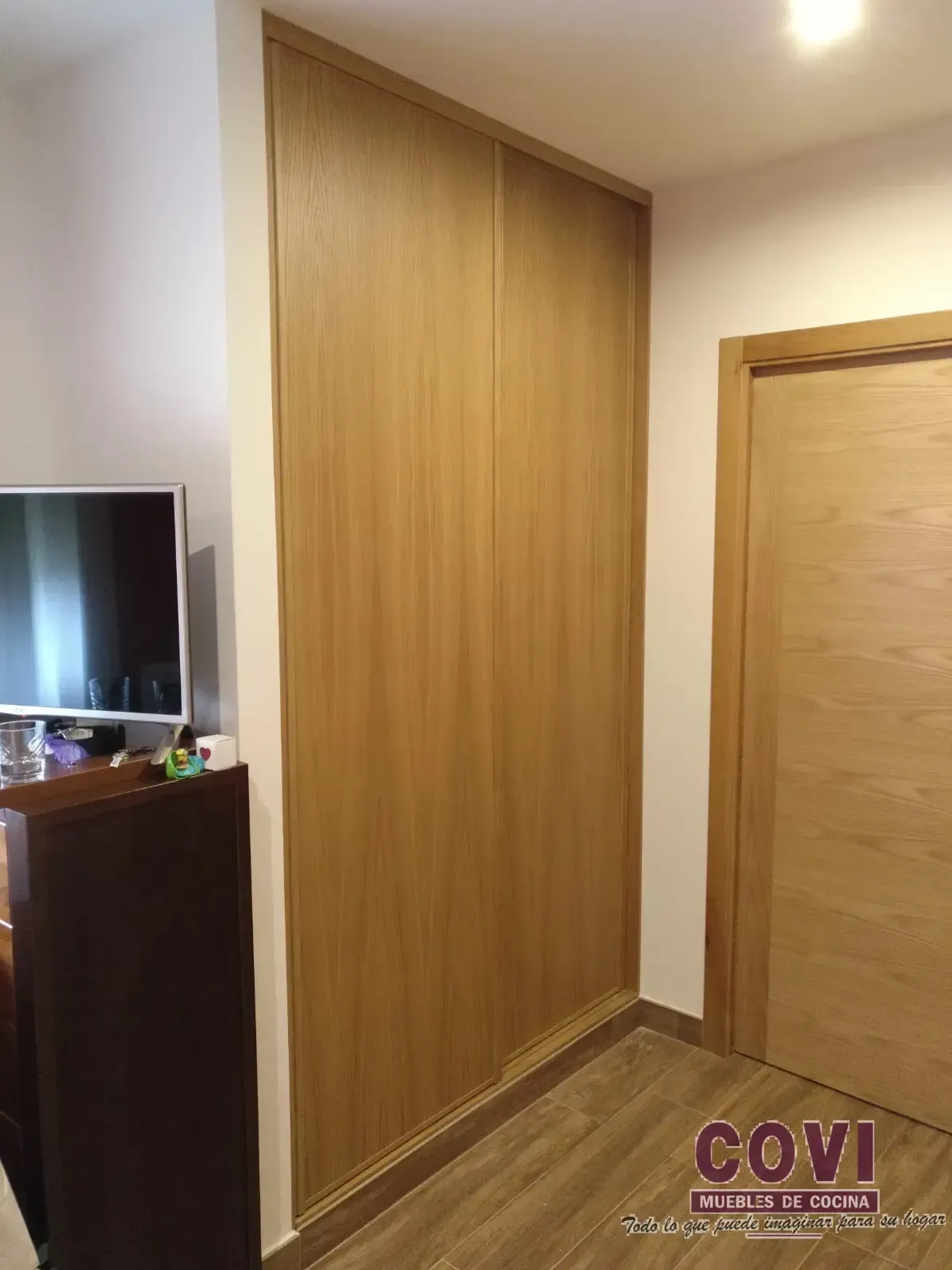 Puertas de armario de madera y puerta en un pasillo con suelo de madera y TV.