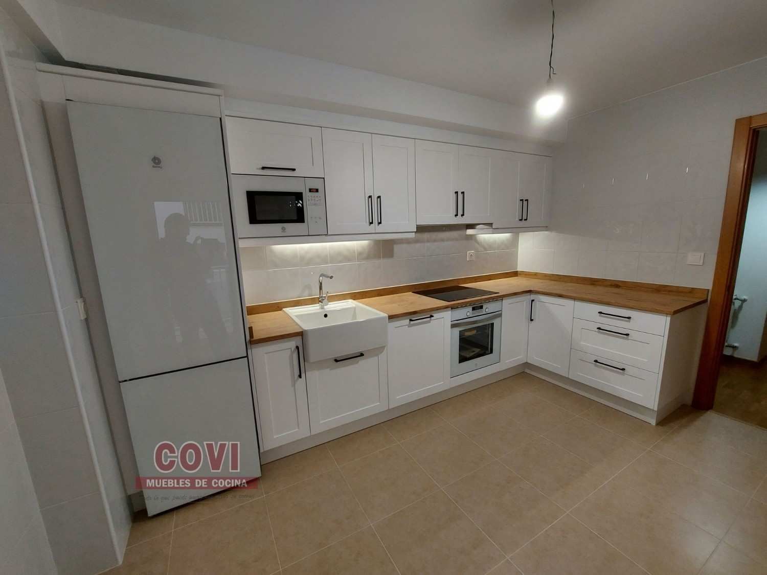 Cocina blanca con encimeras, electrodomésticos y gabinetes de madera.