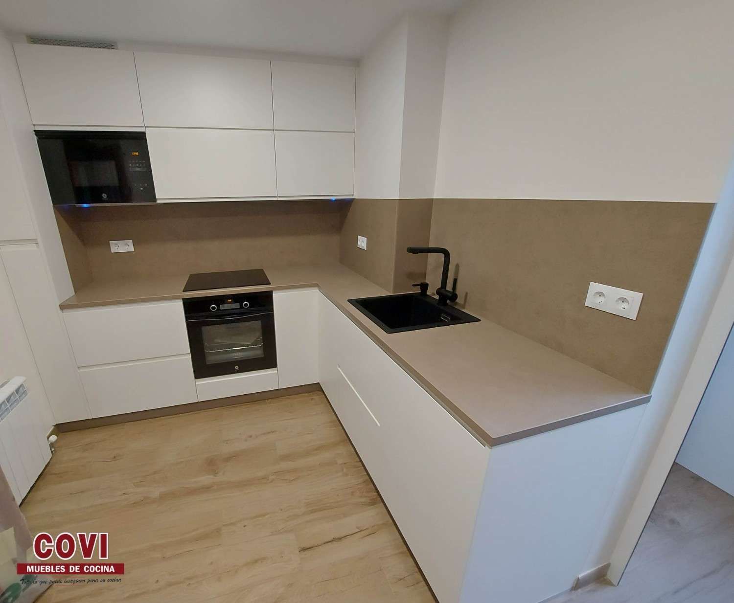 Cocina blanca moderna con microondas y horno incorporados, fregadero y grifo negros.