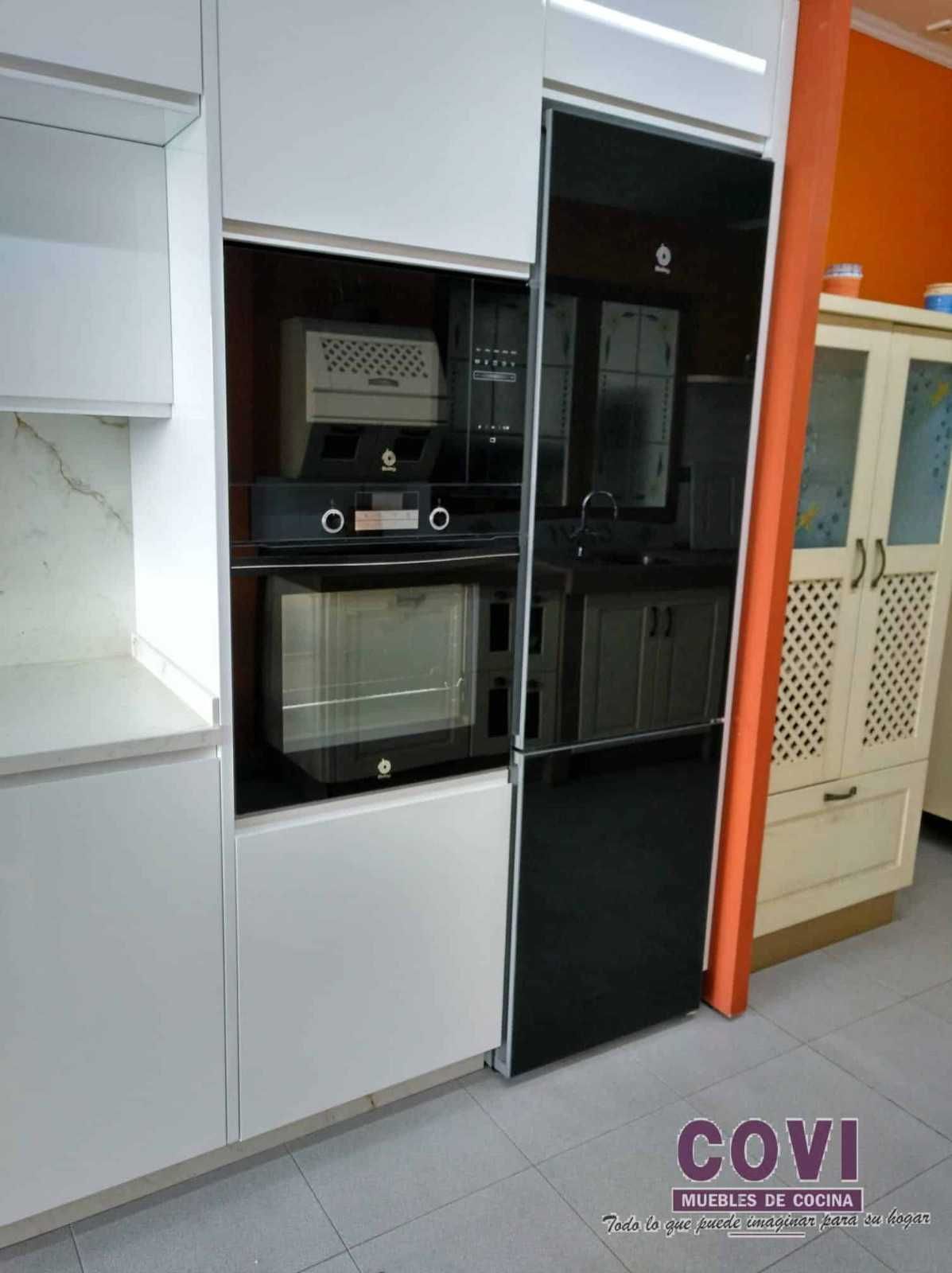 Electrodomésticos de cocina empotrados: horno, microondas y fregadero con armarios blancos y negros. Pared naranja visible.
