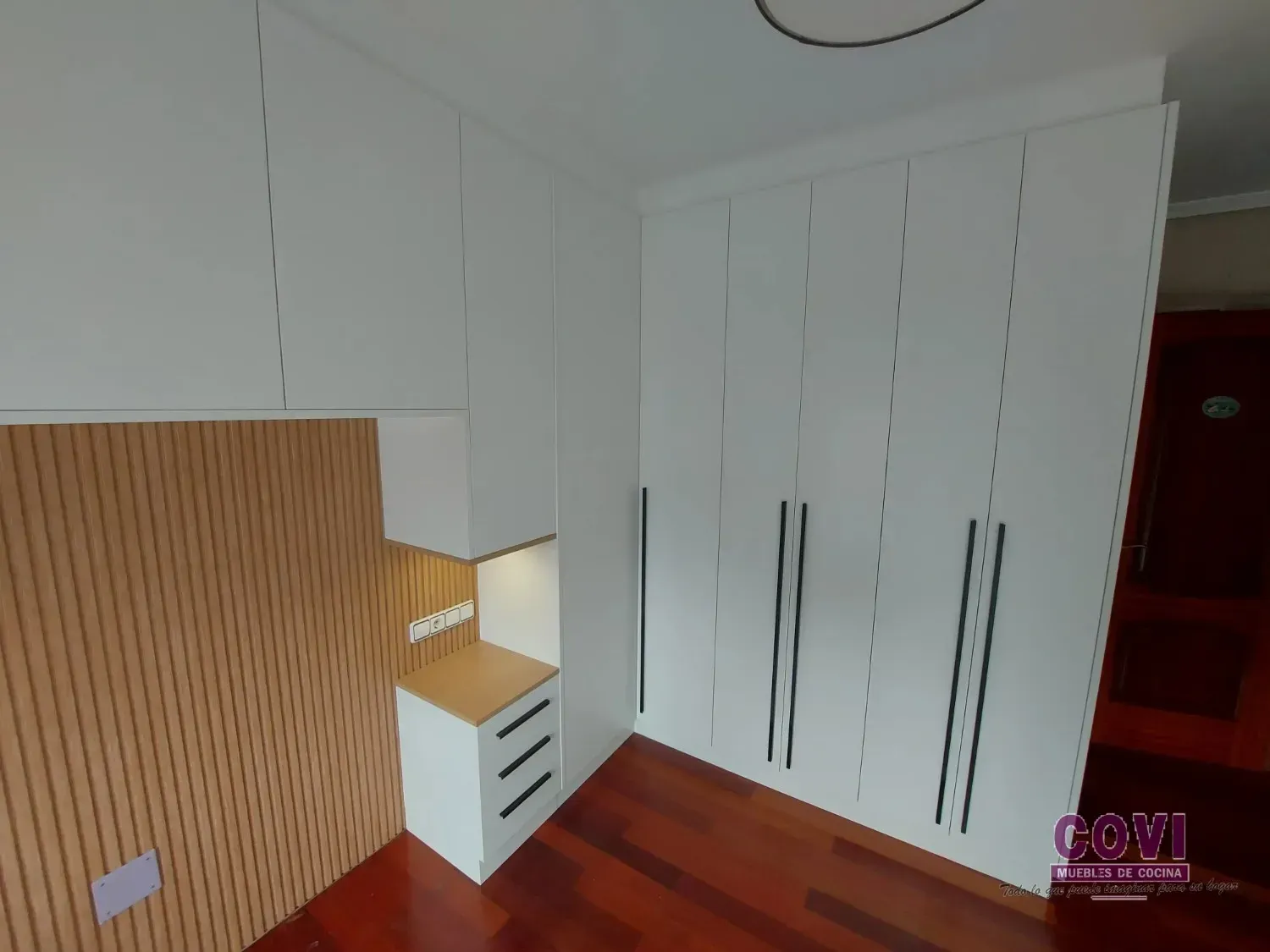 Armario blanco y mesita de noche con cajones. Pared con acento de madera y suelo marrón.