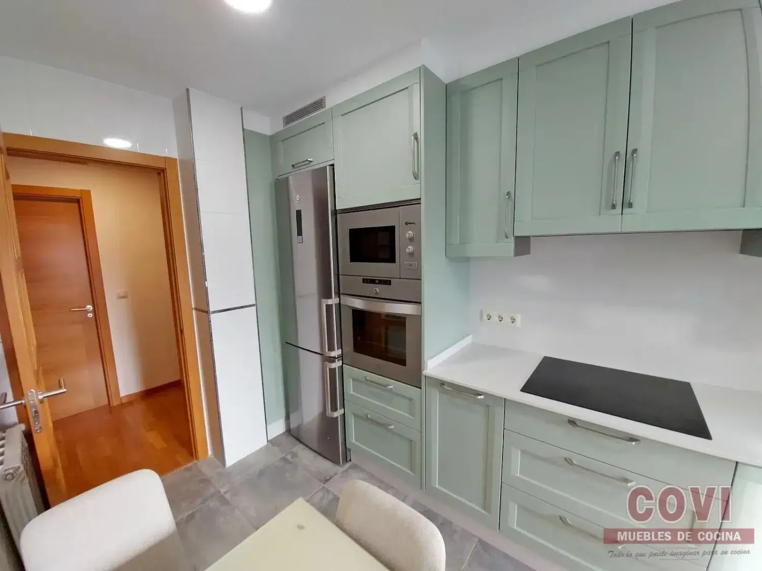 Gabinetes de cocina verdes con electrodomésticos de acero inoxidable, encimera y puerta de color blanco.