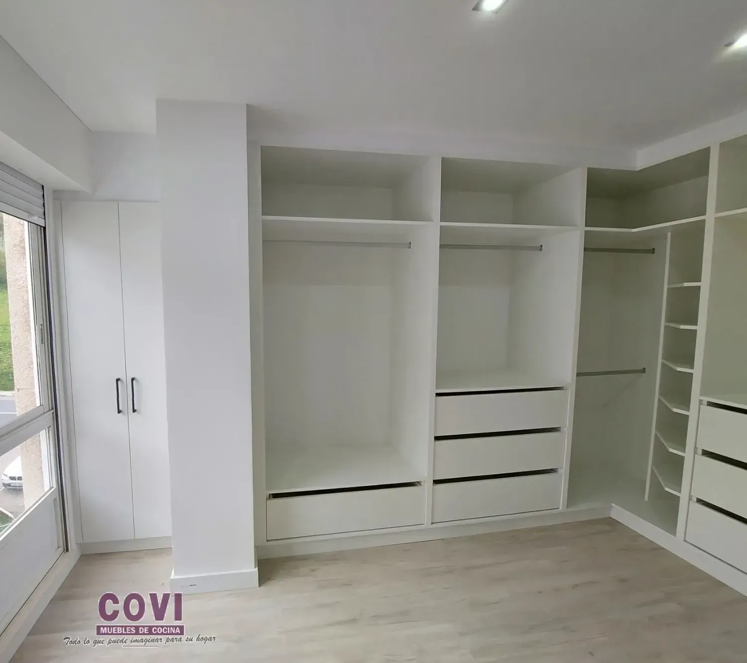 Armario empotrado blanco con baldas, cajones y barras para colgar en estancia luminosa.