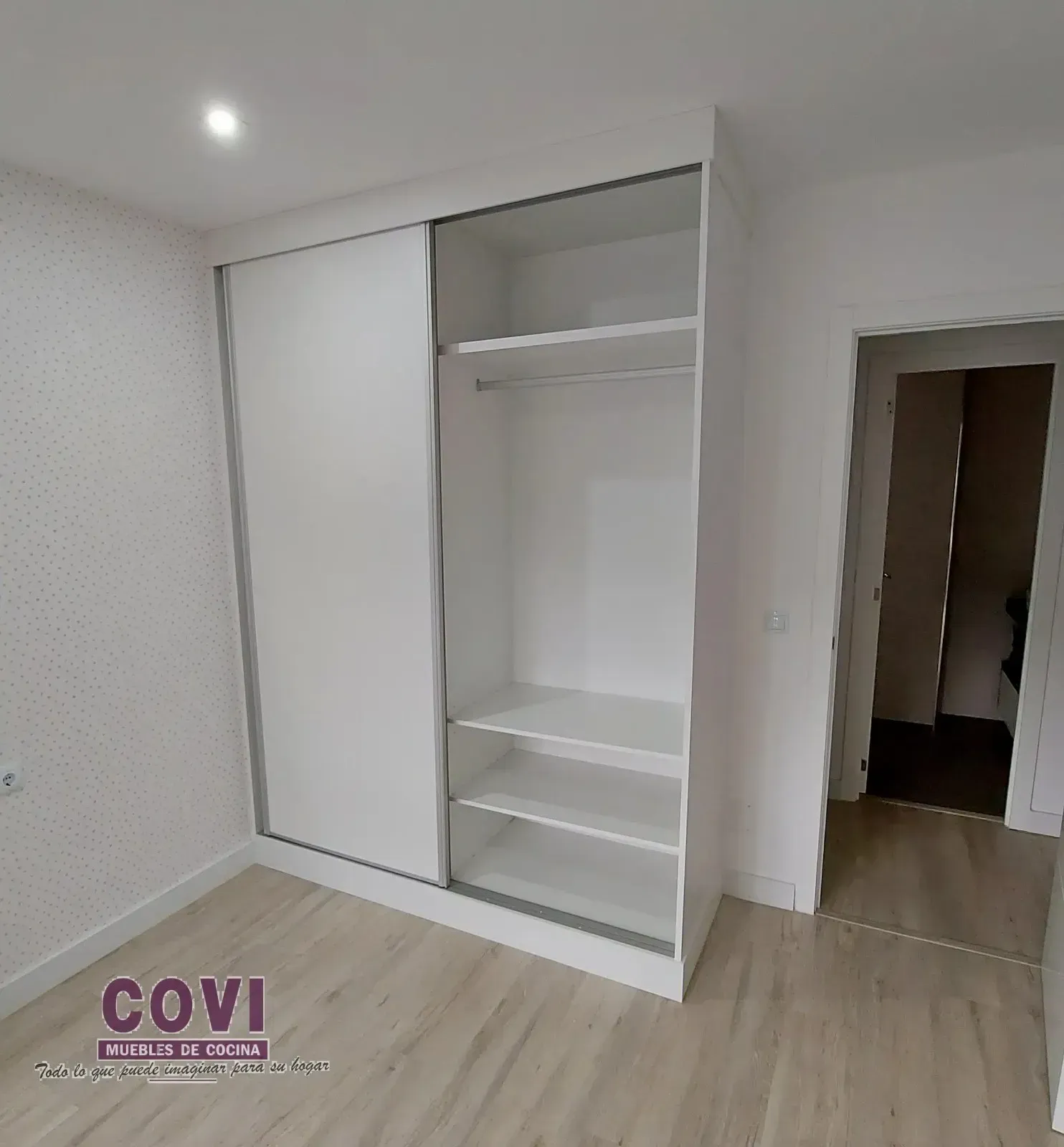 Armario empotrado blanco con puertas correderas, sección abierta con estantes y barra.