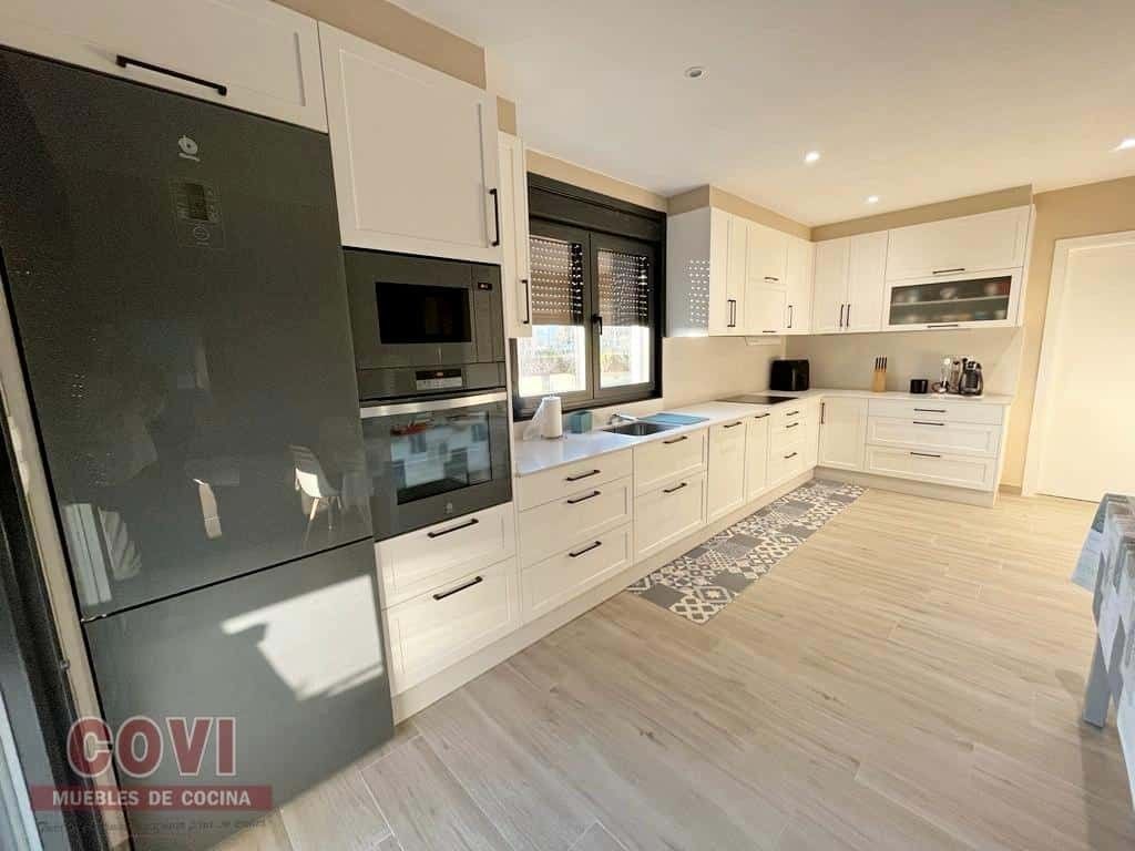 Cocina moderna con gabinetes blancos, refrigerador gris y pisos de madera clara.