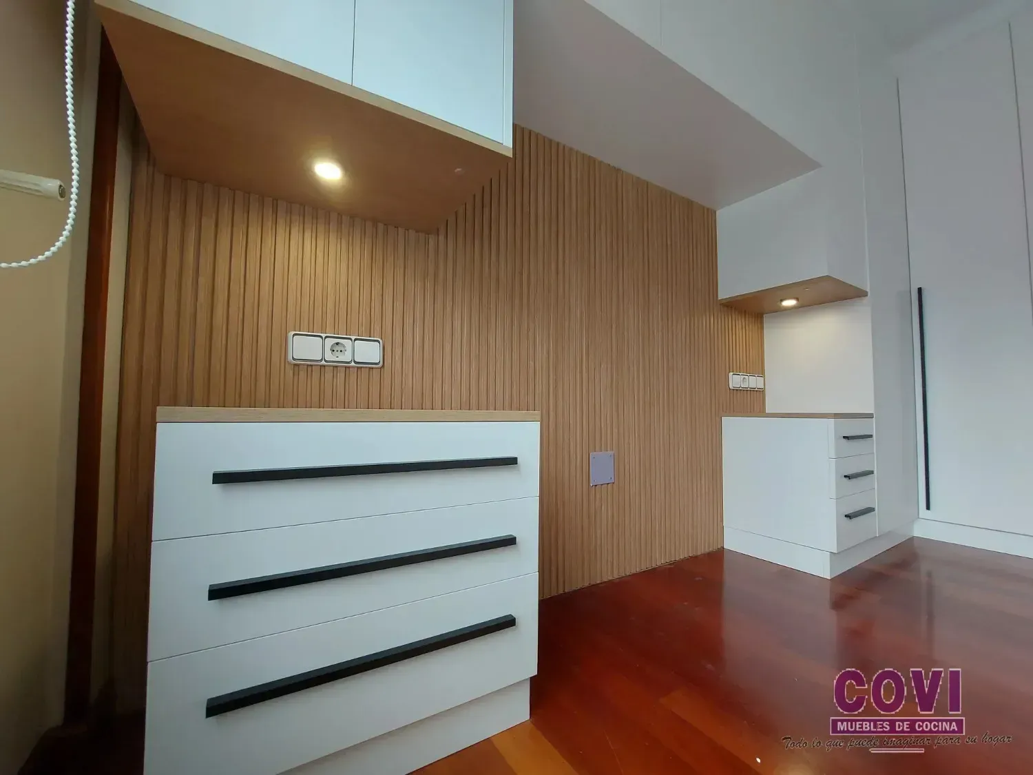 Dormitorio moderno con paneles de madera, cajones blancos y piso de madera.