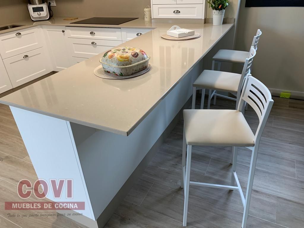 Cocina blanca con encimera, taburetes y un pastel.