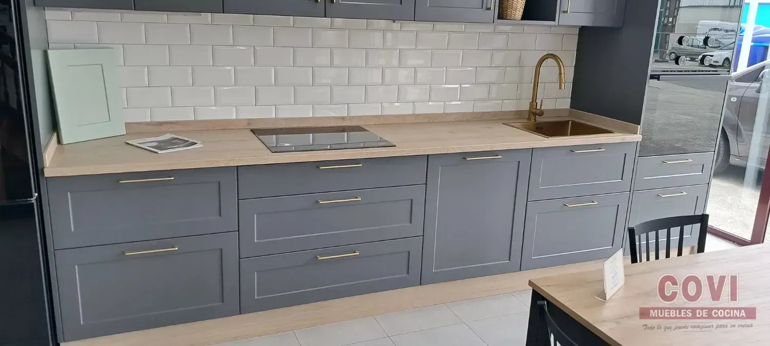 Una cocina gris con una encimera de color claro, salpicadero blanco y grifo dorado.