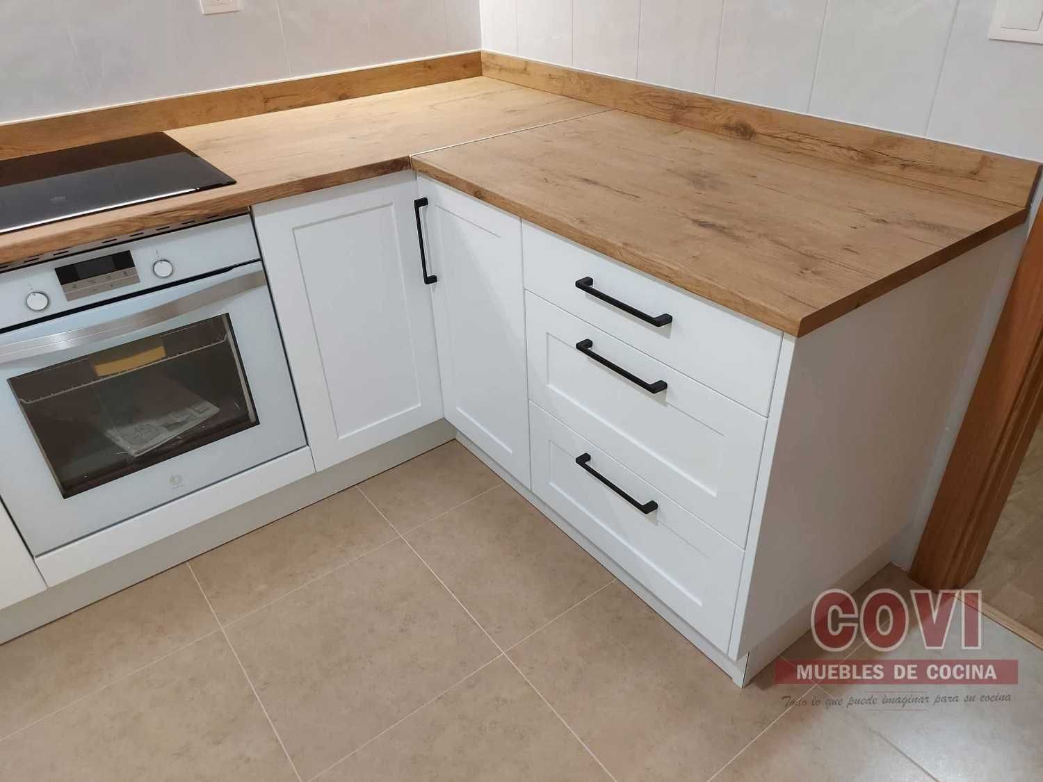 Gabinetes de cocina blancos con encimera de madera y herrajes negros. Horno y placa de cocina visibles.