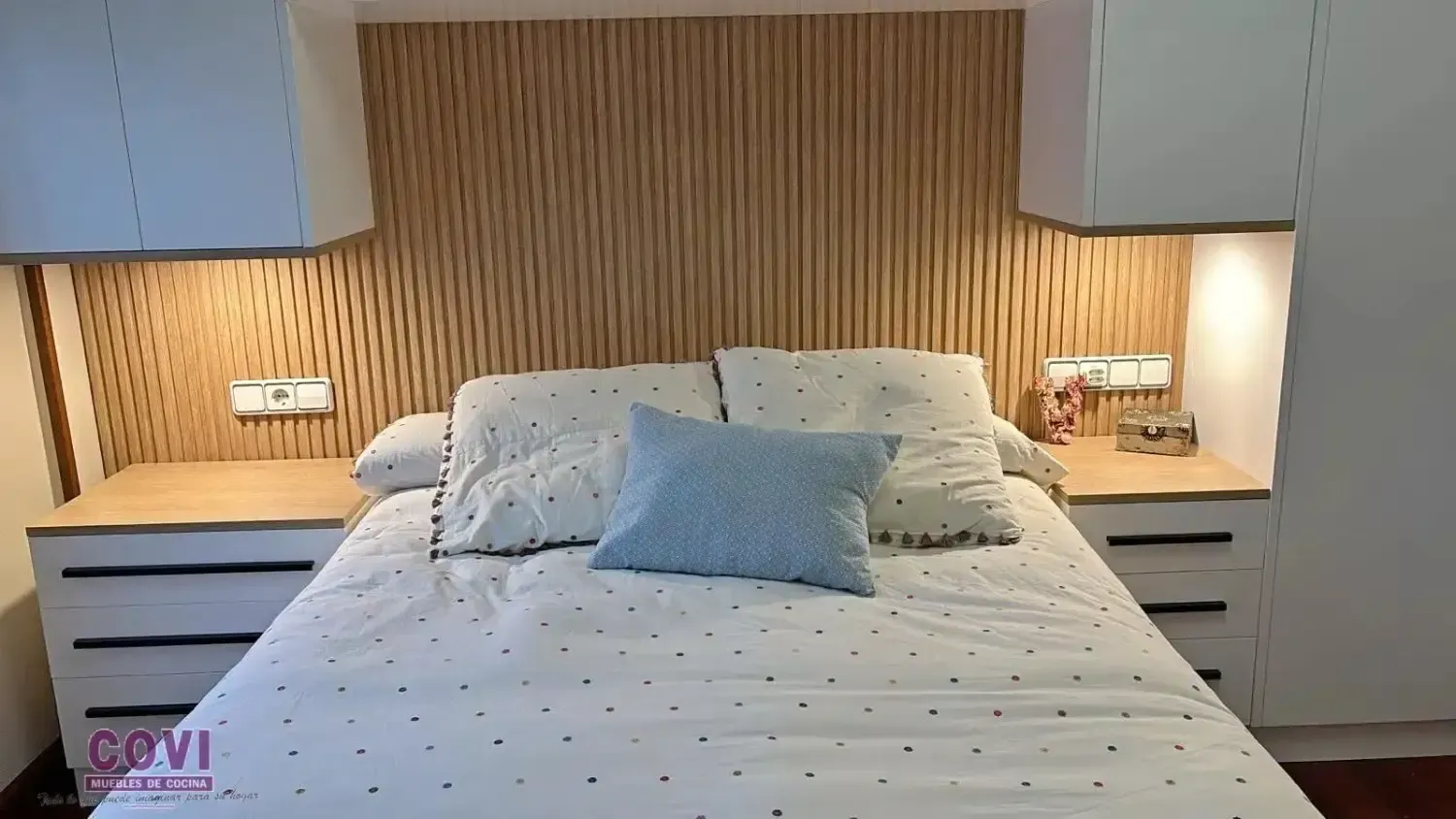 Dormitorio con cama blanca, cabecero de madera, mesitas de noche y muebles altos.