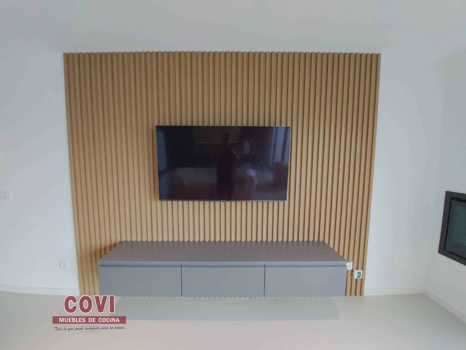 Revestimiento de madera con un televisor montado y una consola multimedia flotante de color gris.