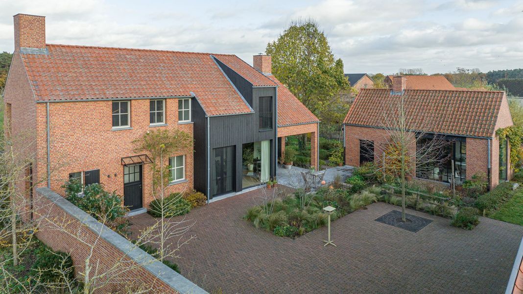 Bakstenen huis met rood pannendak en glazen entree, omgeven door een grindbinnenplaats en bloembedden.