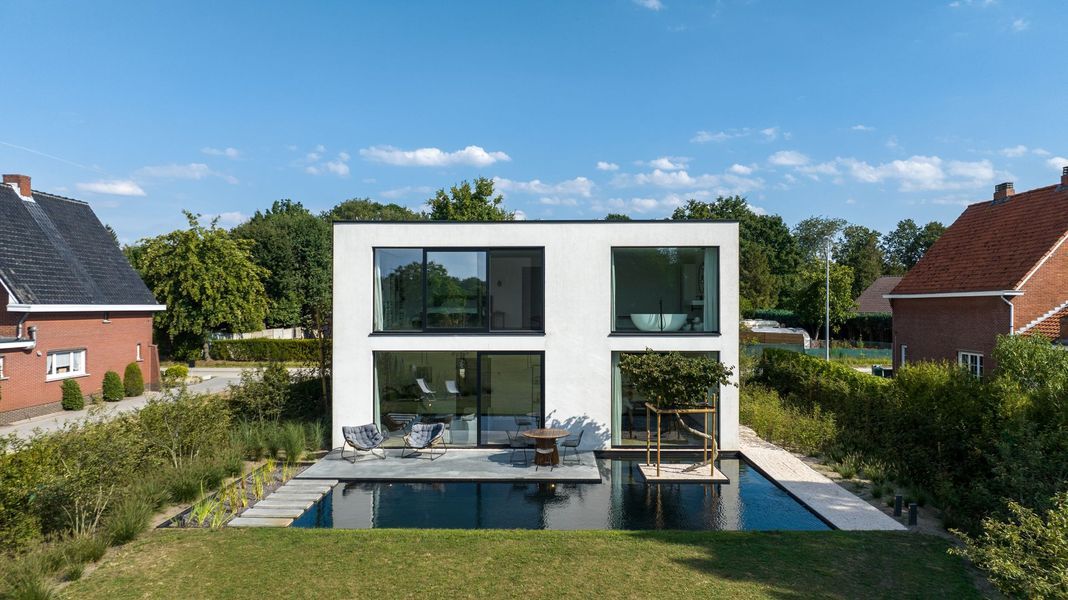 Moderne witte woning met twee verdiepingen, grote ramen, terras en zwembad in een groene tuin in een buitenwijk.