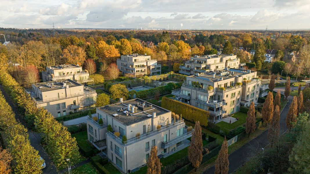 Luchtfoto van moderne appartementencomplexen omgeven door bomen in het herfstlicht.