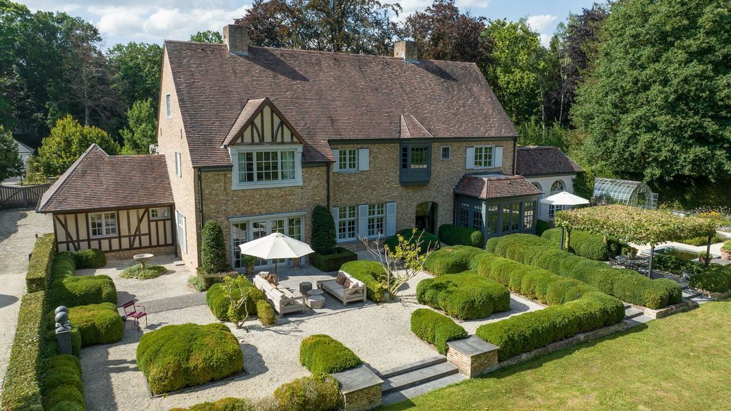 Groot stenen huis met een pannendak, aangelegde tuin, terras met zitgelegenheid en een vrijstaande garage op een zonnige binnenplaats.