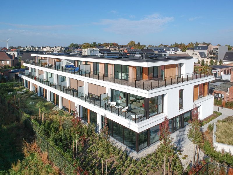 Modern wit appartementencomplex met glazen balkons en dakterrassen in een woonwijk.